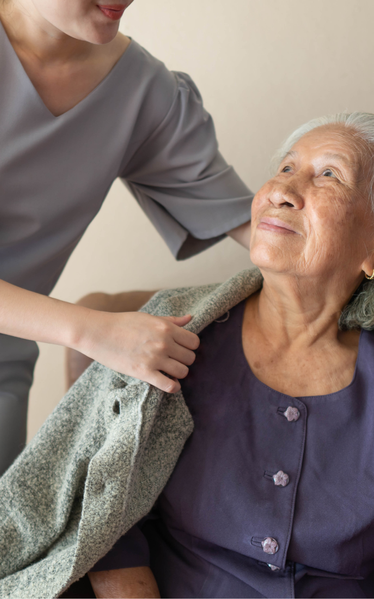 A home care recipient smiles at her caregiver as she helps her put her coat on.