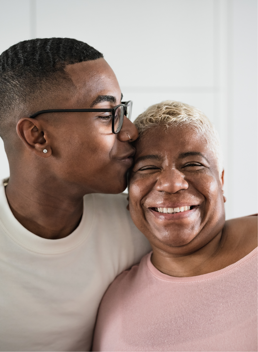 Young man kisses older woman on the head while she smiles for a photo.