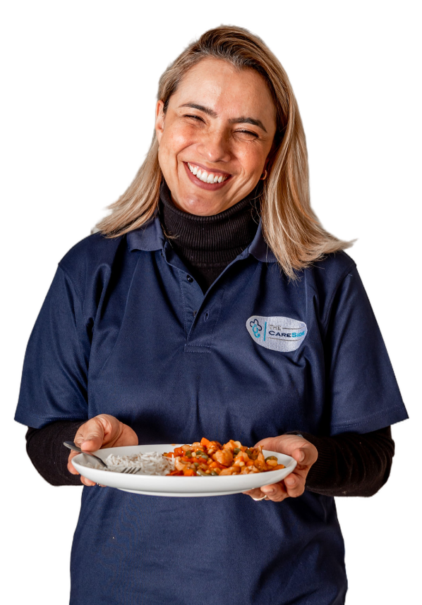 A caregiver from The CareSide smiles and holds a plate of food.