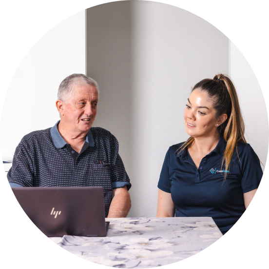 Home care client sitting next to his caregiver as they look at a computer on the table.