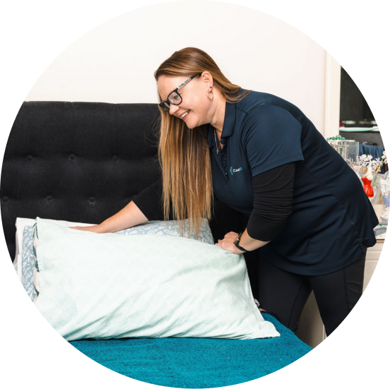 Caregiver from The CareSide provides post-hospital support while arranging the pillows on a bed.