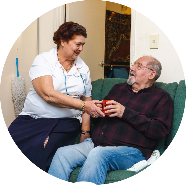 A caregiver from The CareSide provides home care in Sunshine Coast while handing her client a cup of tea as he relaxes on a sofa.