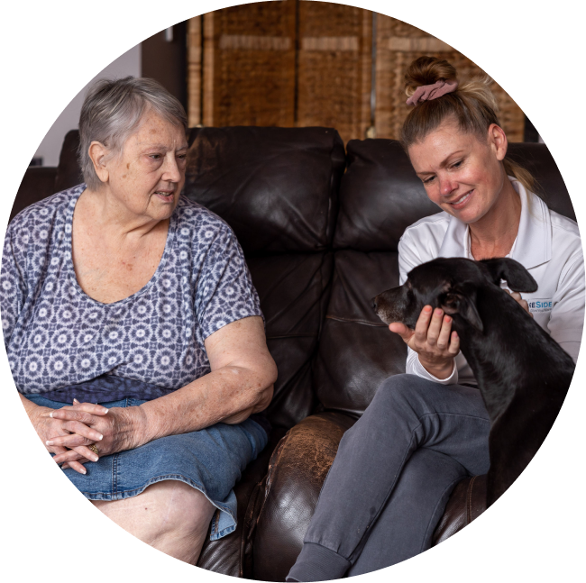 A caregiver from The CareSide provides home care services in Hobart while chatting with her client and petting her dog.