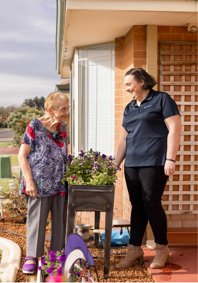 A caregiver from The CareSide provides home care services in Brisbane while helping her happy client plant flowers outside.