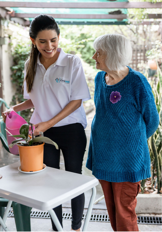 A home care recipient smiles at her caregiver from The CareSide as they water plants outside.