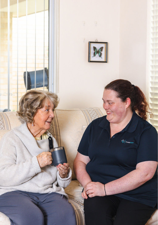 Home care Sunshine Coast recipient shares a funny story with her caregiver from The CareSide while they sit on a sofa.