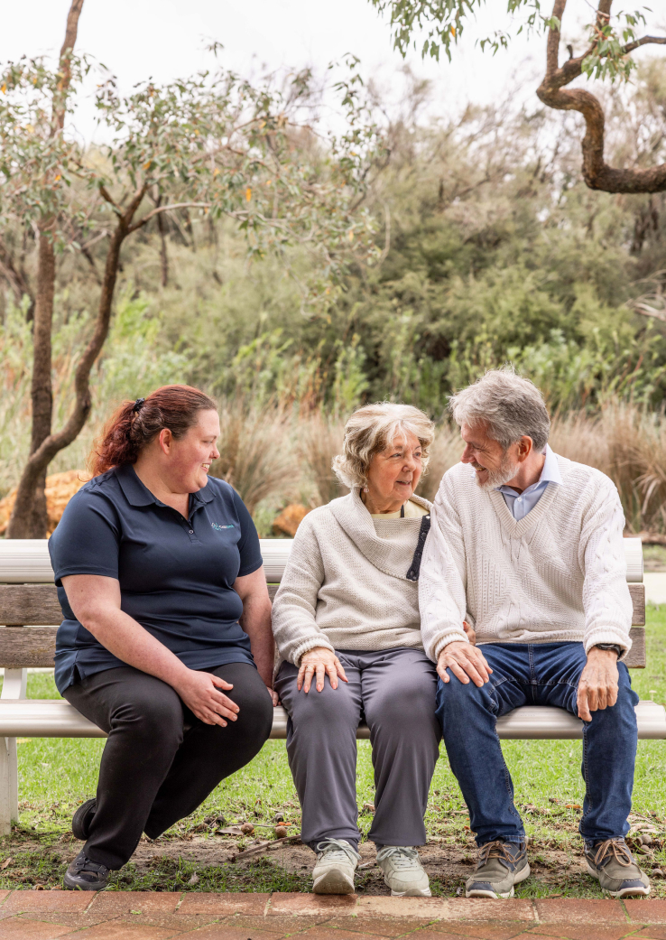 A caregiver from The CareSide sits on a park bench next to home care recipients.