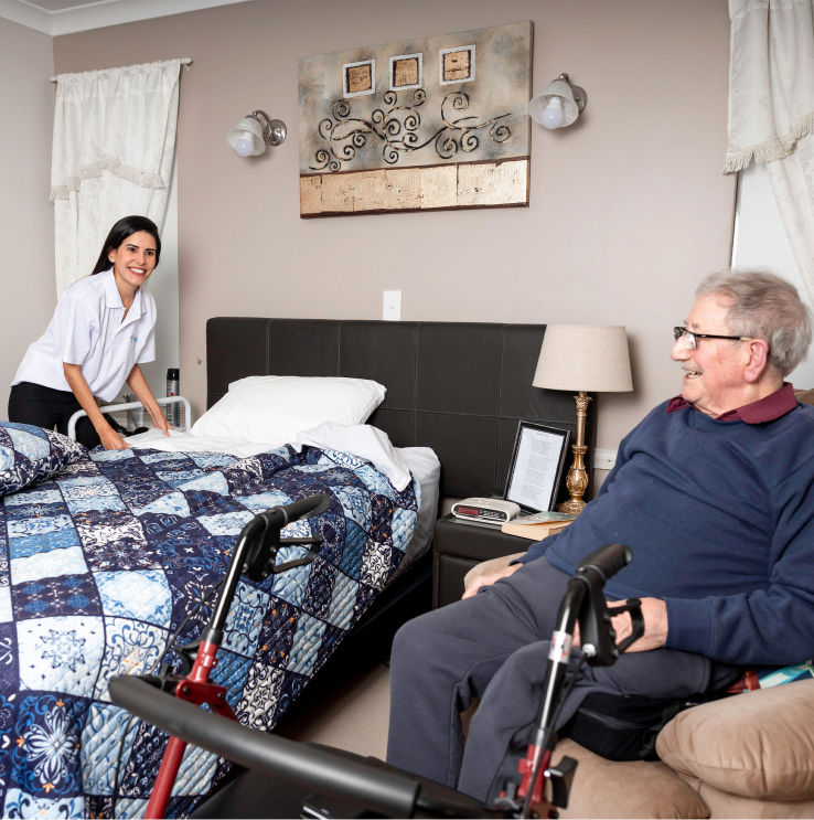 Overnight care recipient smiles as his caregiver from The CareSide makes the bed.