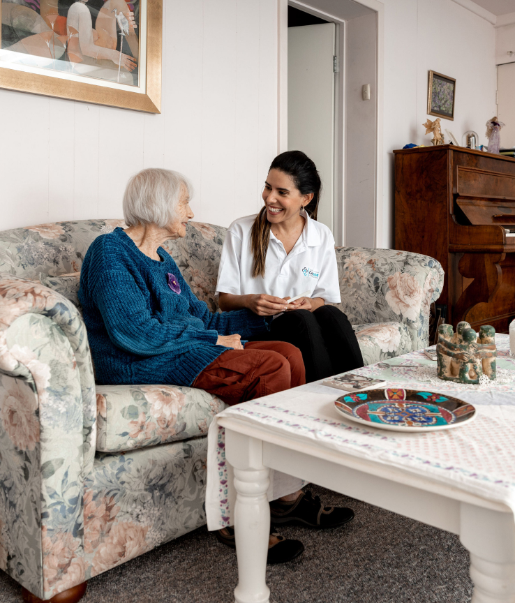 Caregiver from The CareSide providing 24-hour care support while sitting next to her happy client on a living room sofa.