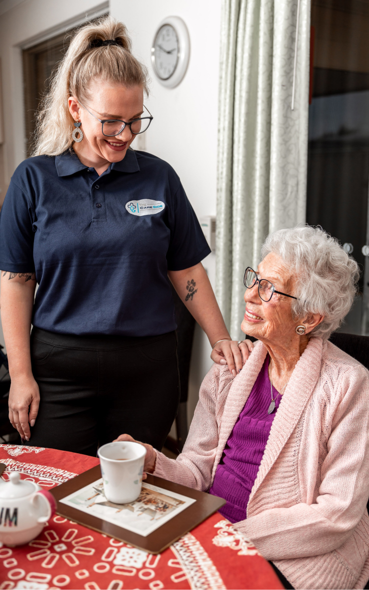 A home care recipient smiling up at her friendly caregiver from The CareSide.