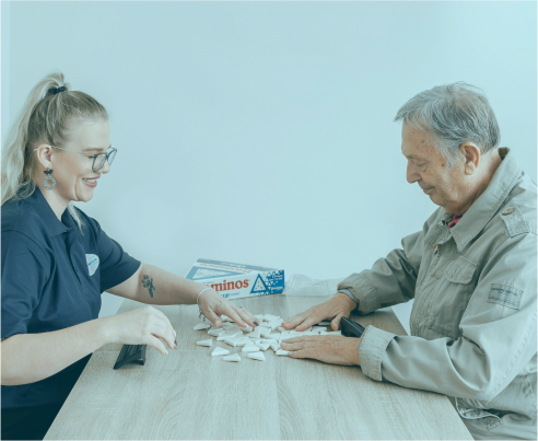 Happy home care recipient plays dominos with his companion caregiver from The CareSide.