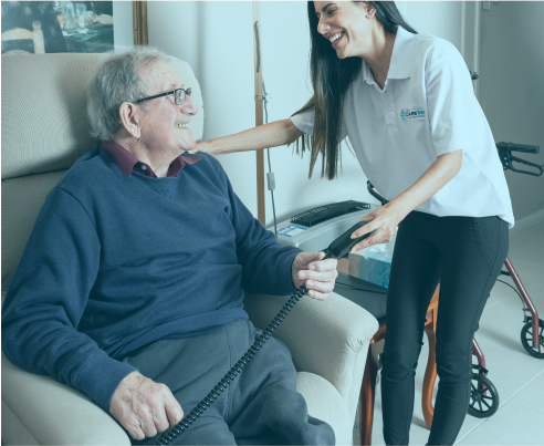 Home care recipient sits in a chair while his smiling caregiver from The CareSide checks in on him.