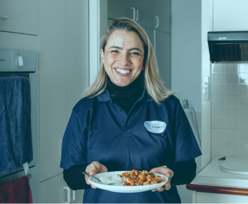 Home care professional smiles for a photo while holding a plate of food.