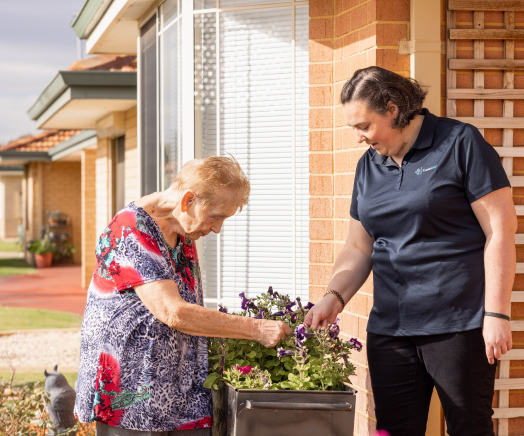 Live-in care recipient works on a flower bed outside with assistance from her caregiver.