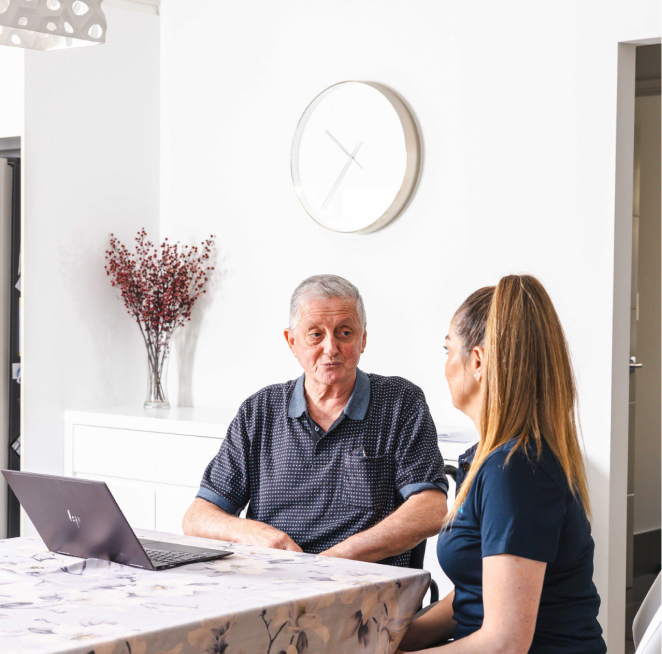 A personal care recipient sits at a table and chats with his caregiver.