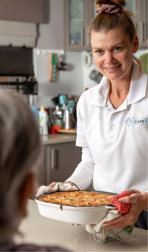 A caregiver from The CareSide holding a hot dish from the oven, which she has prepared while providing personal care support for her client.