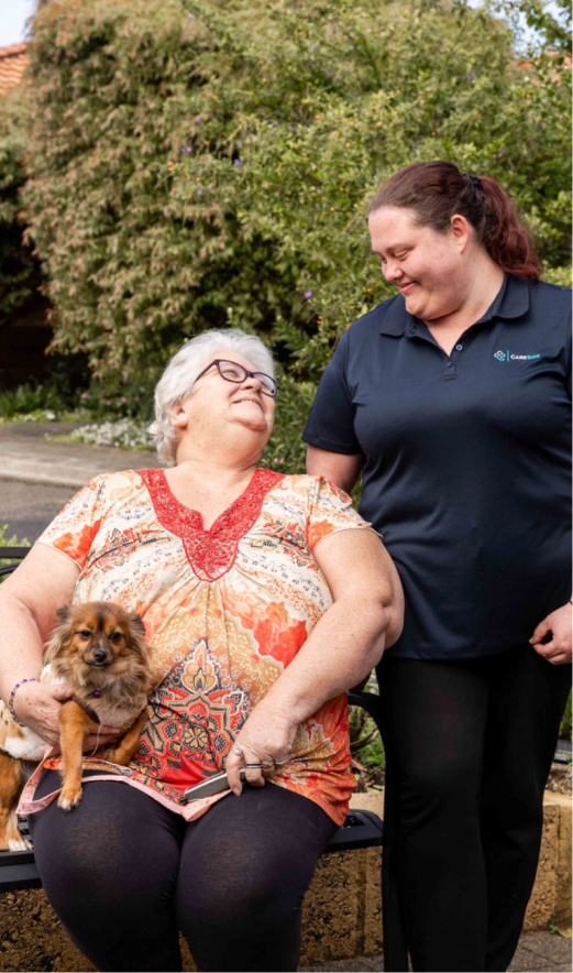 A home care client looking up and smiling at her caregiver standing next to her.