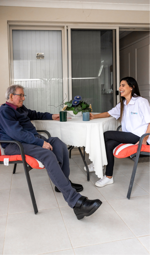 Companion care client and his caregiver share a laugh while drinking coffee and sitting at a table.