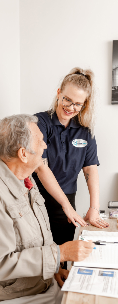 A caregiver from The CareSide checks in on her client, who smiles up at her while sitting at a table.