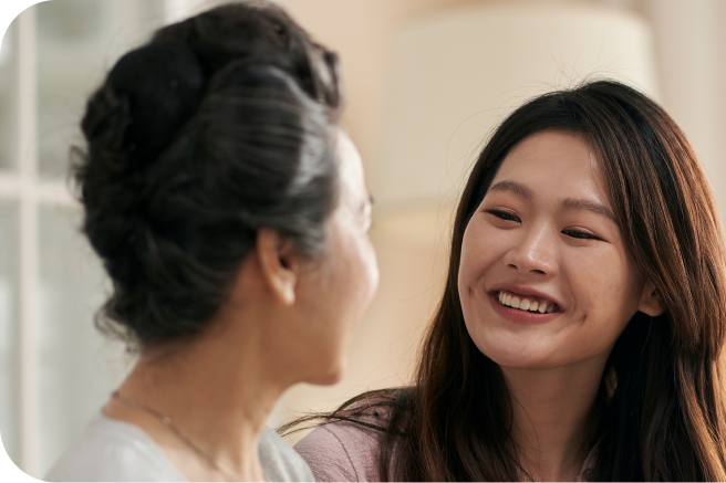 A photo of a young woman smiling while she talks to her parent about aged care.